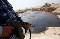 Policeman stands guard near oil that leaked from a damaged pipeline in Basra