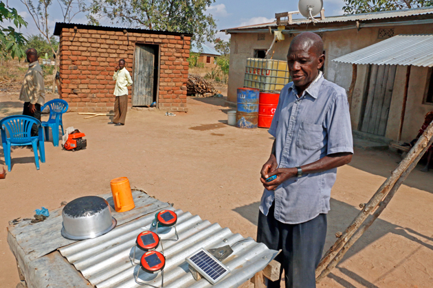 Lusela Murandika is happy to have made the jump from diesel generator to solar. The panel that powers his TV is on the roof behind him, behind the satellite dish.