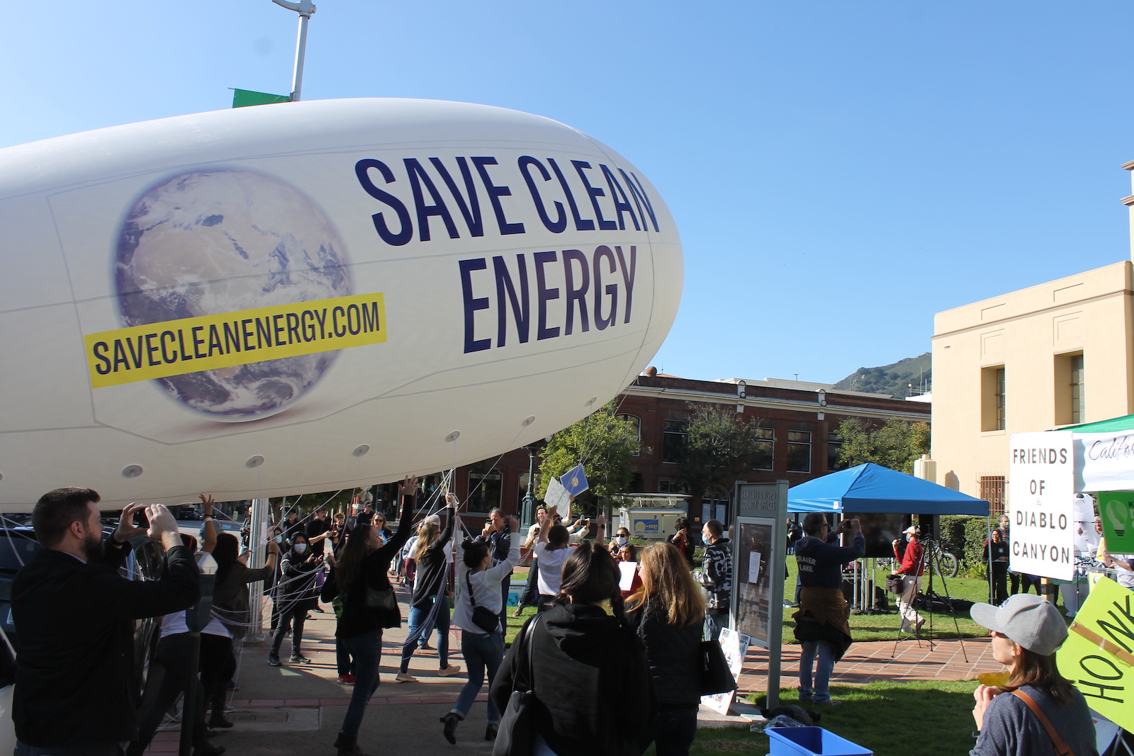 environmental activists pull a blimp with the words "save clean energy" printed on the side