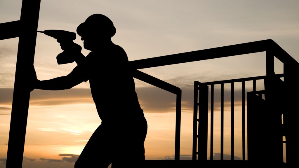 A construction worker uses a drill as he works on a building frame.