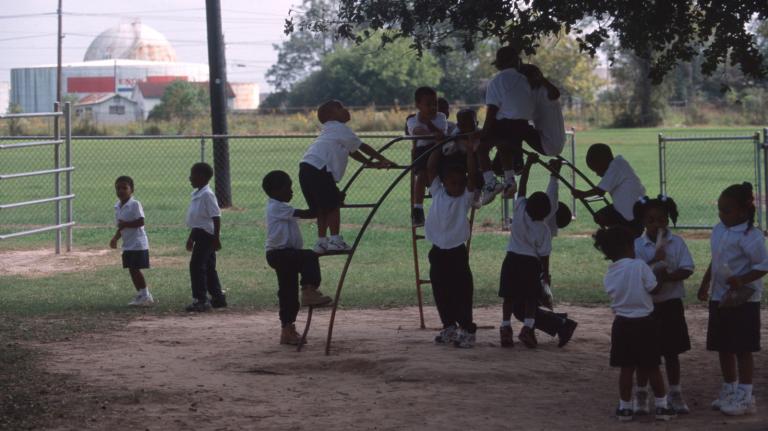 Black children in playground with Exxon refinery in background