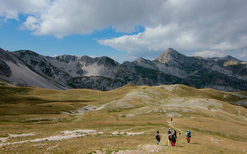 Eine Gruppe von Wanderern geht durch die Rasenfläche mit der Bergkette in der Ferne