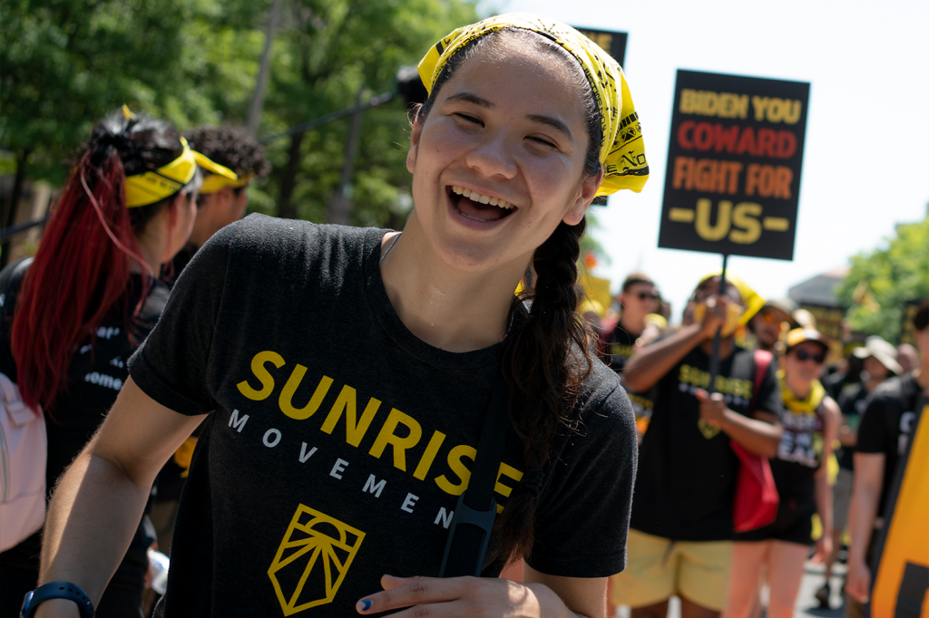 Audrey Lin, wearing a Sunrise Movement shirt and yellow bandana, smiling at a protest