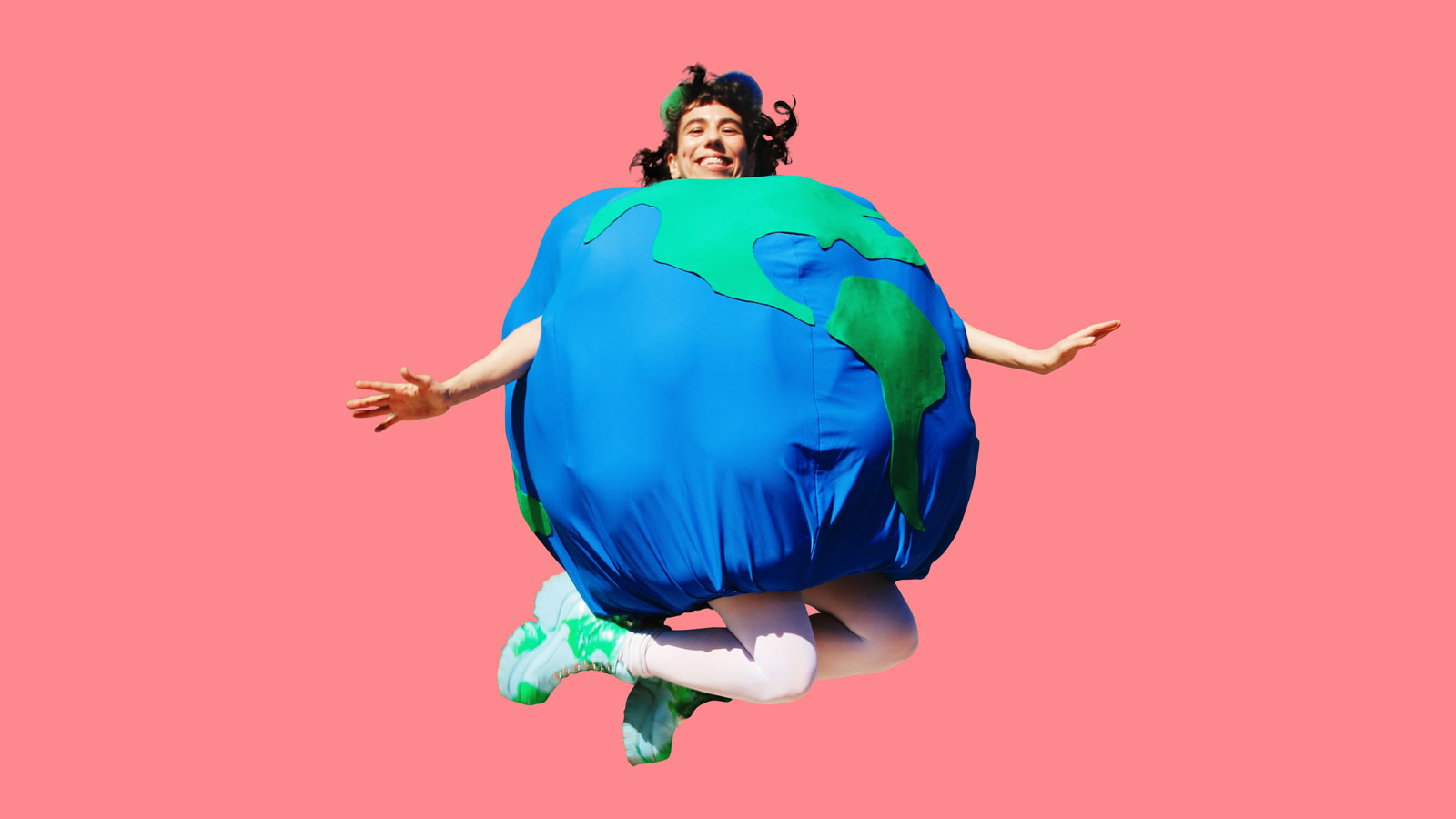 Hila dressed as the earth jumping against pink background