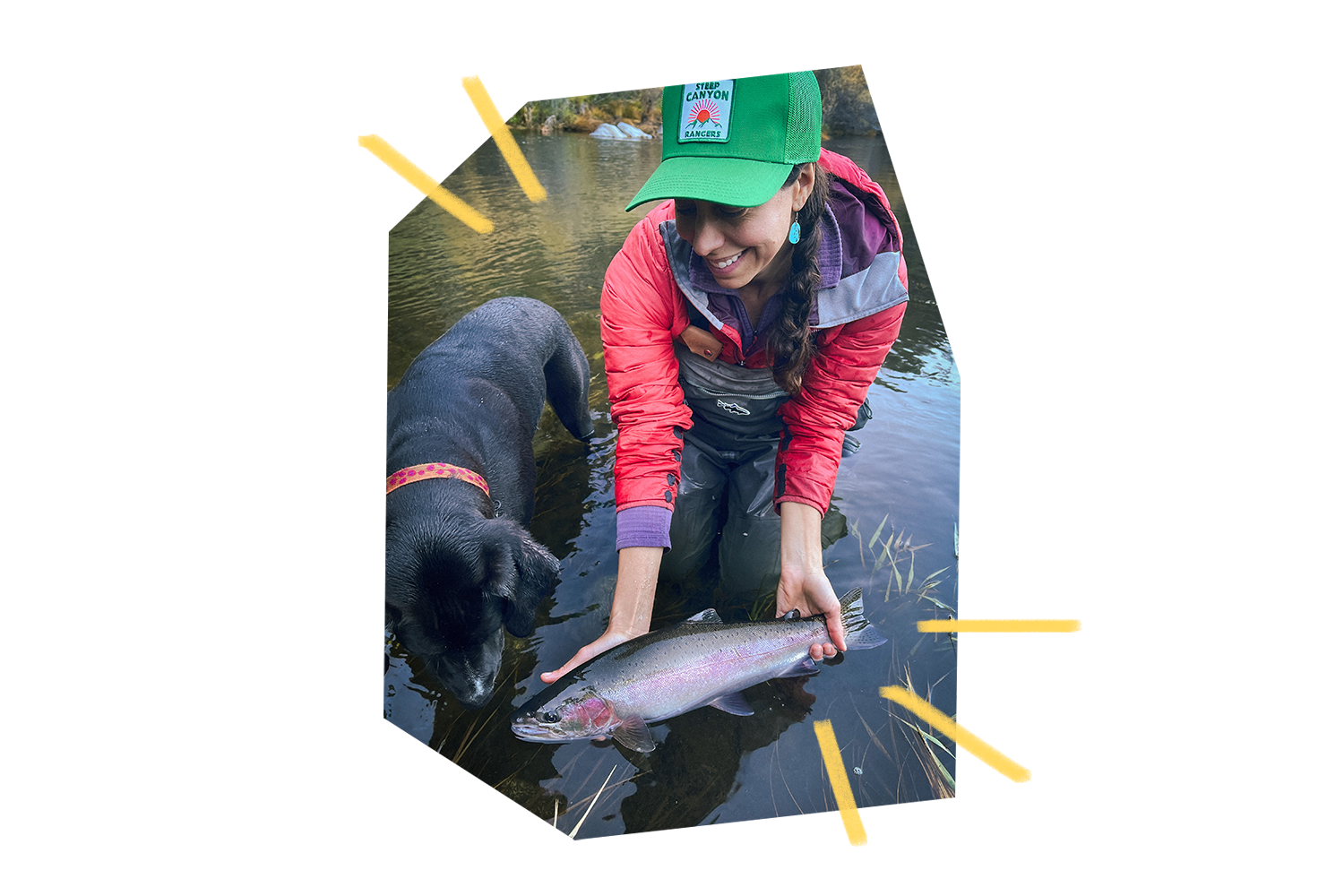 Katie holding fish above water's surface with dog beside her