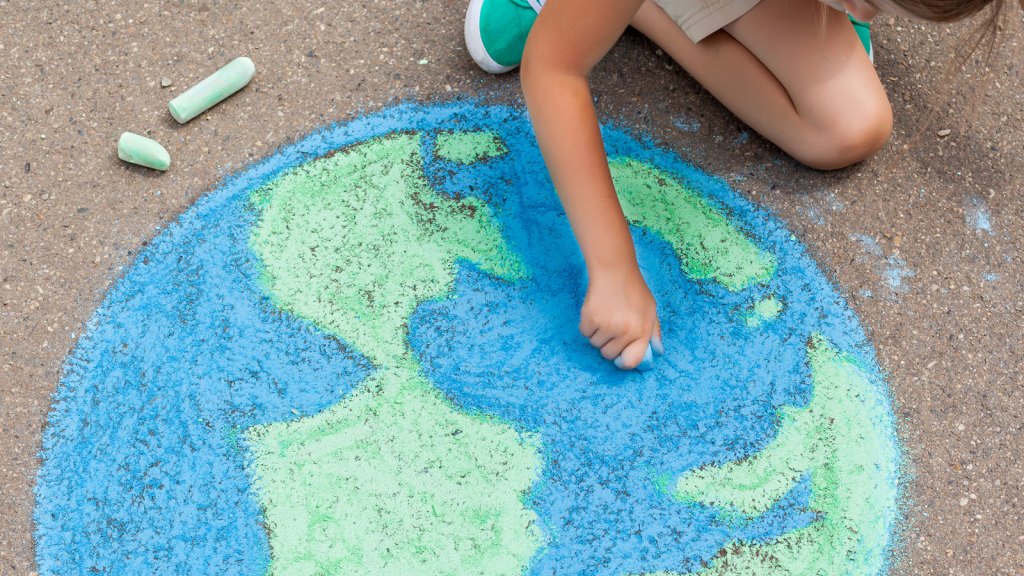 Child draws the earth with blue and green chalk on asphalt
