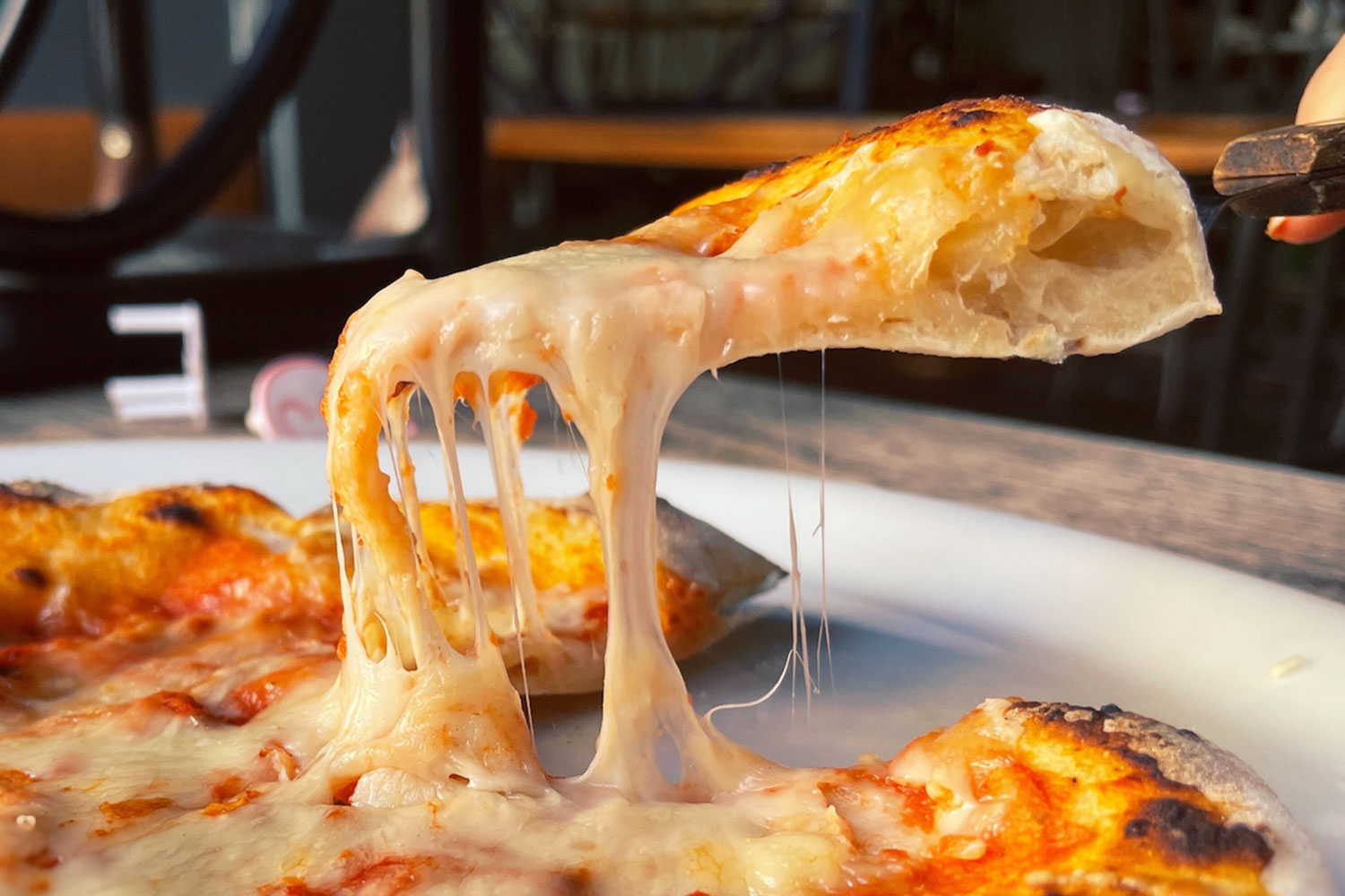 Slice of cheese pizza is lifted with pie server, strings of cheese stretching from it