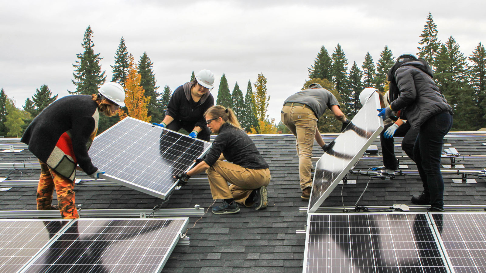 Students standing on top of a mock roof install solar panels
