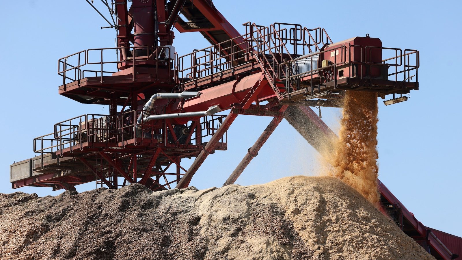 A towering pile of sawdust beneath machinery at a wood pellet mill.