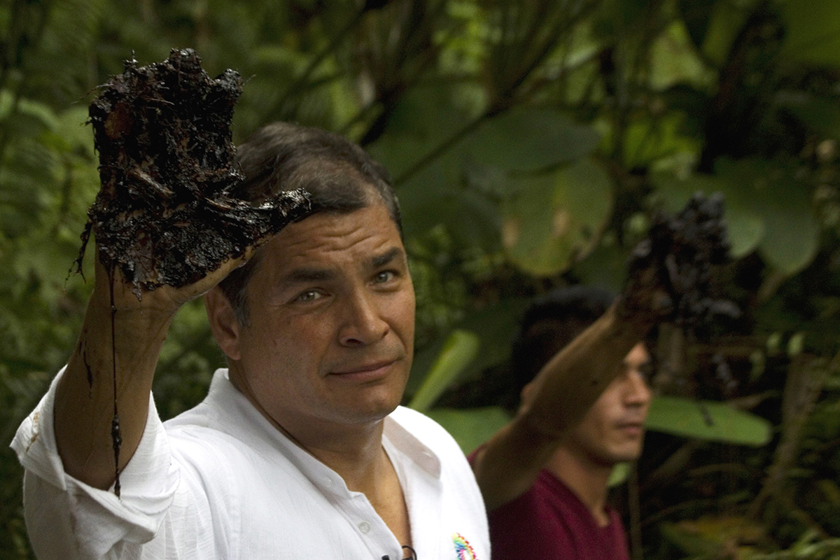 Ecuador's President Rafael Correa raises an oil-coated hand.
