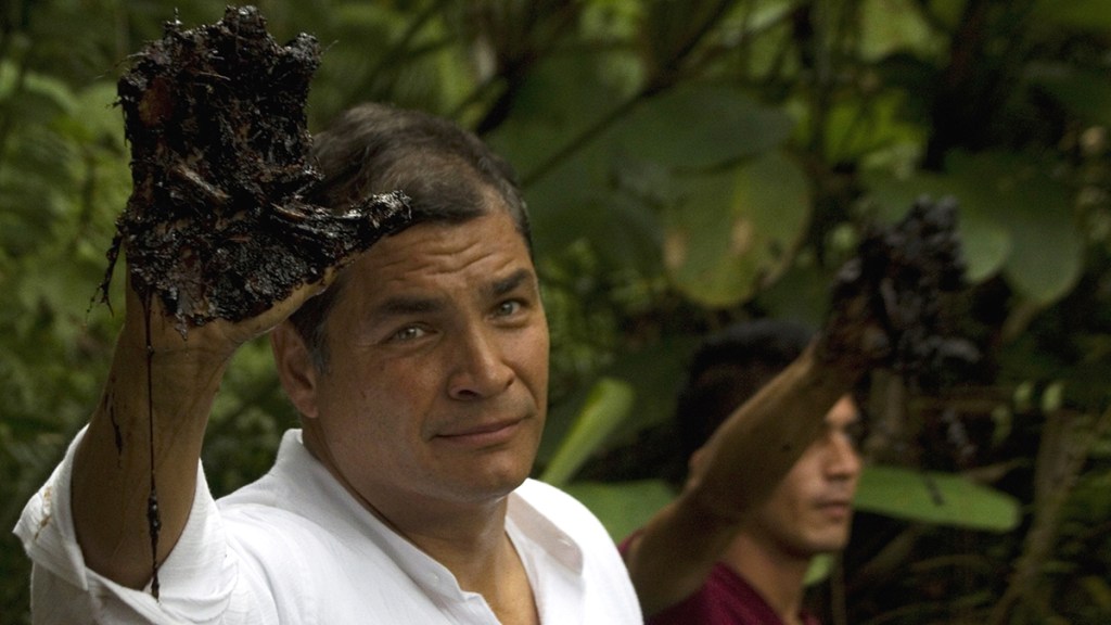 Ecuador's President Rafael Correa raises an oil-coated hand.