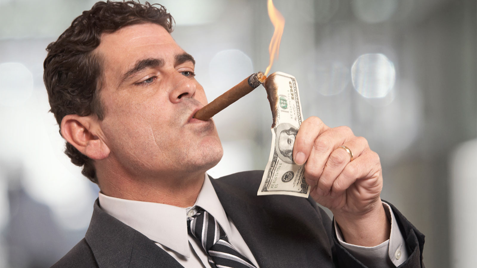 Man lighting cigar with $100 bill