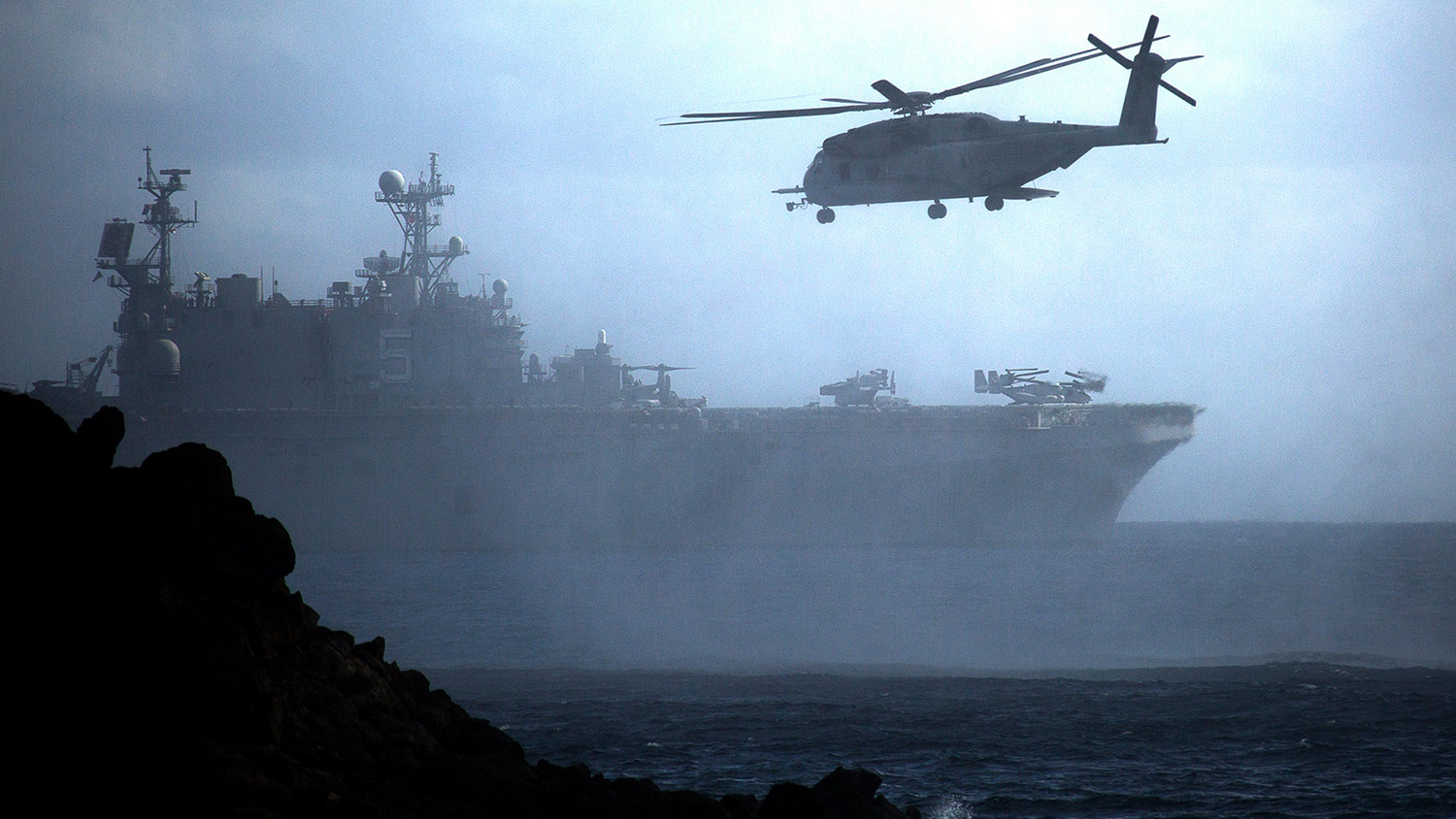 A CH-53E Super Stallion helicopter flies ahead of the amphibious assault ship USS Peleliu (LHA-5) after conducting helocast operations at Pyramid Rock Beach, Marine Corps Base Hawaii.