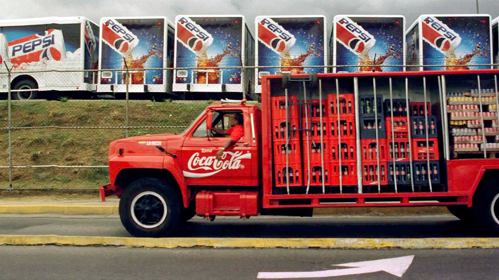 A Coca Cola truck passes in front of a Pepsi Co. parking lot filled with new Pepsi Cola trucks