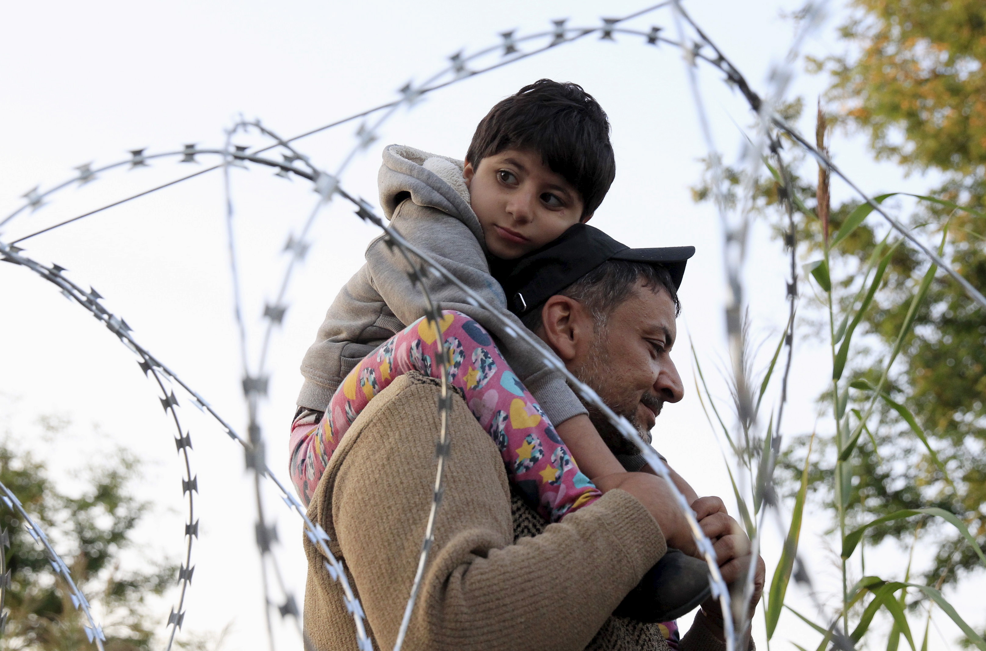 A Syrian migrant with a boy, on the Serbian side of the border with Hungary, walks behind a razor wire near Roszke, Hungary August 28, 2015.