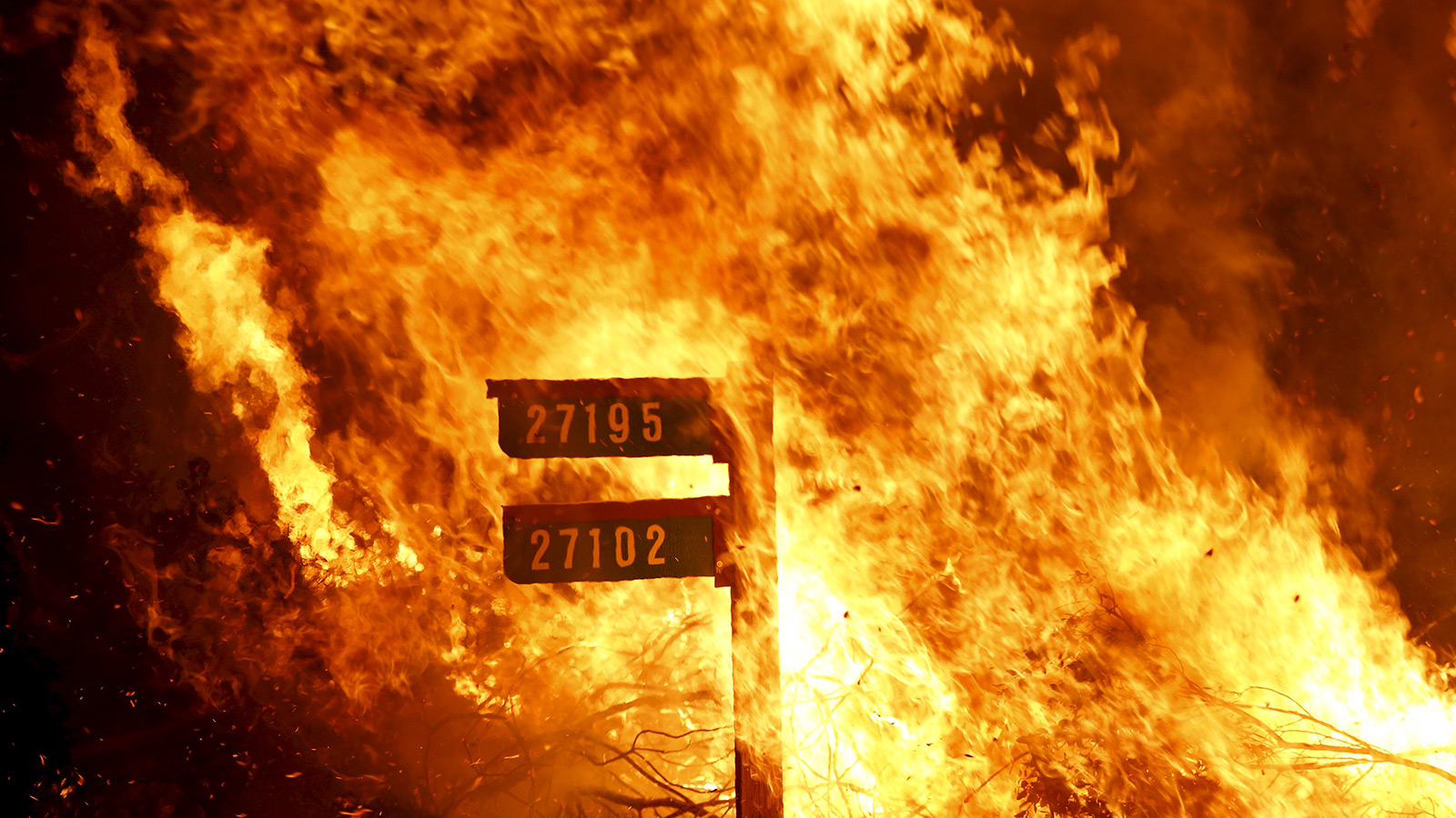 Flames from the Jerusalem Fire consume a sign containing addresses to homes along Morgan Valley Road in Lake County, California