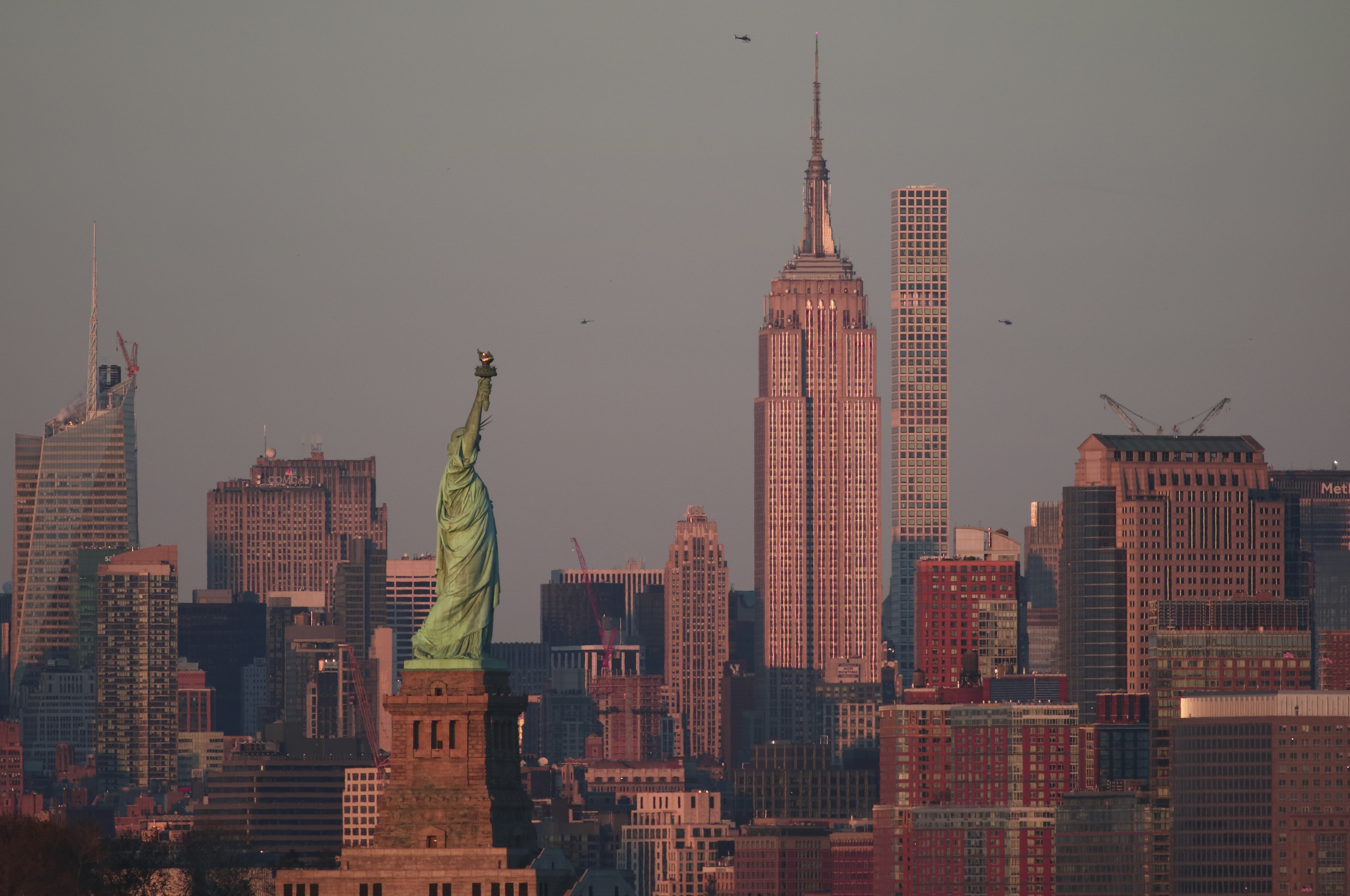 The sun sets on the Empire State Building and Statue of Liberty in New York City.