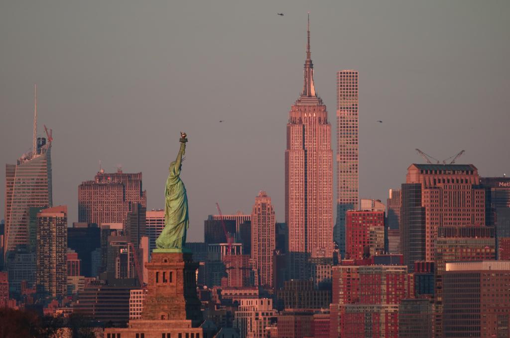 The sun sets on the Empire State Building and Statue of Liberty in New York City.