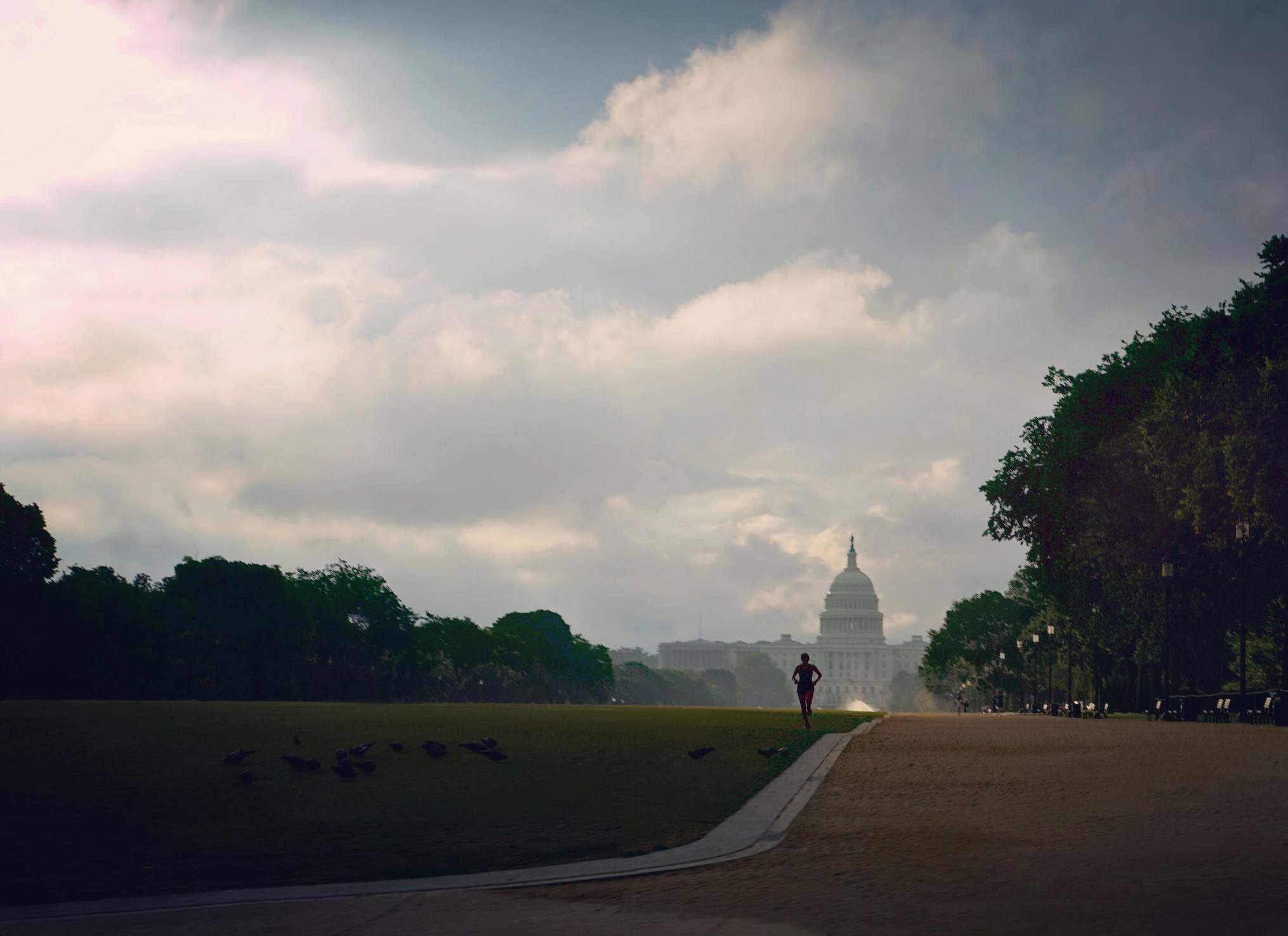 A man runs on a field against a cloudy sky, with the United States Capitol in the background.