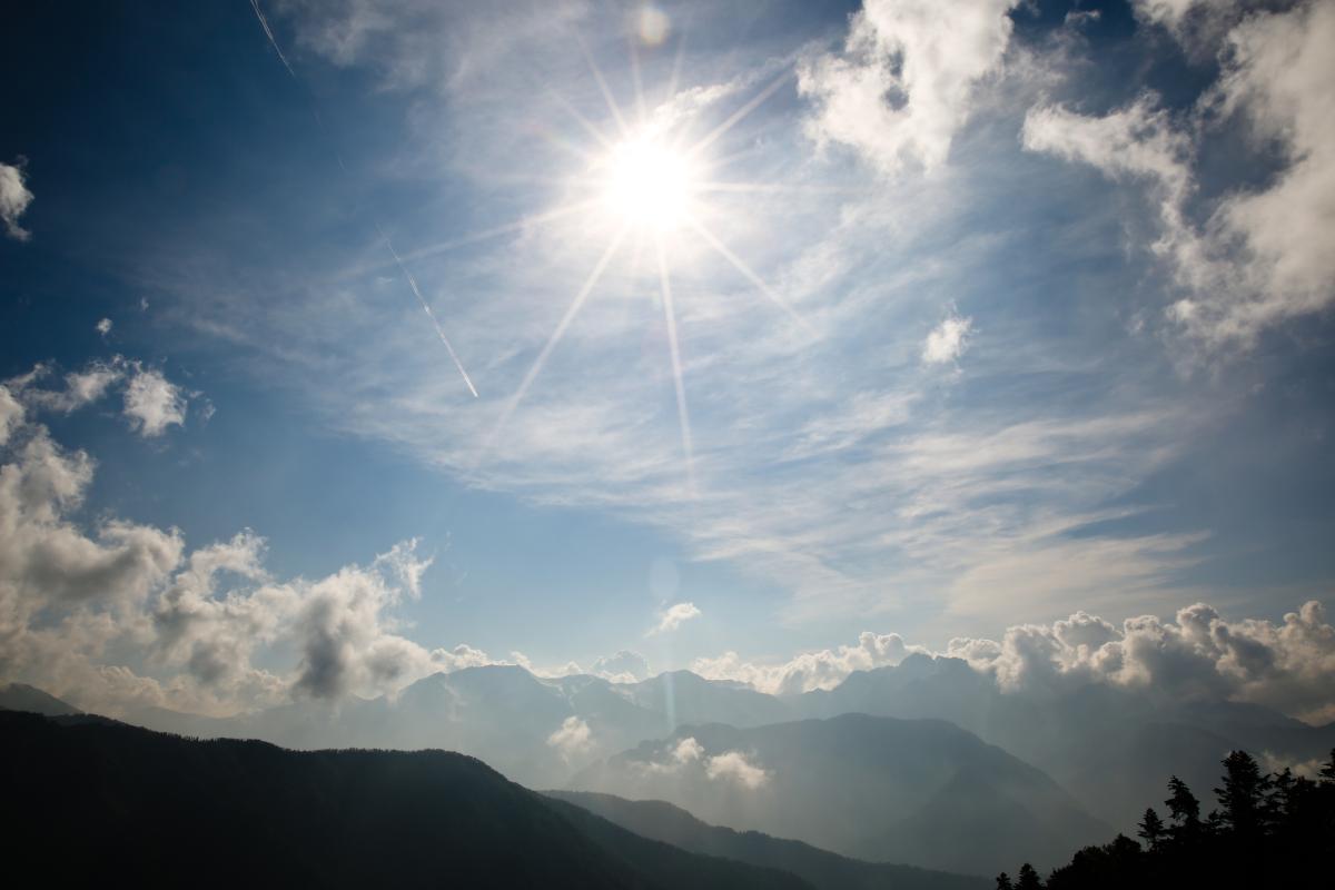 A view of the sun and clouds over mountains.