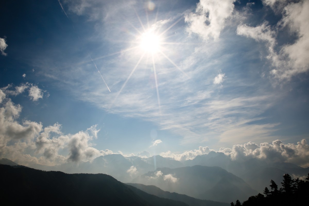 A view of the sun and clouds over mountains.