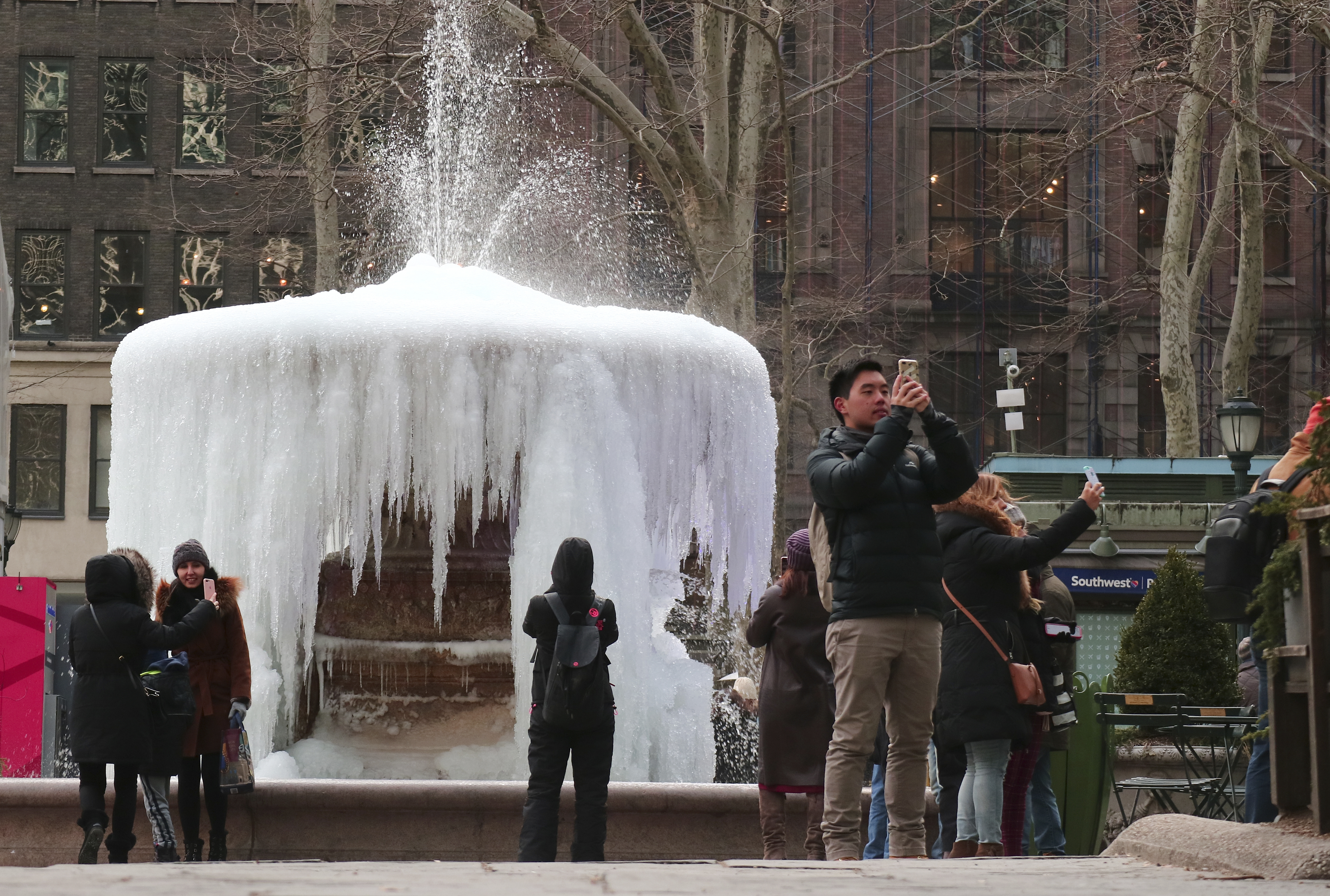 People take selfies in front of frozen fountain in New York City.