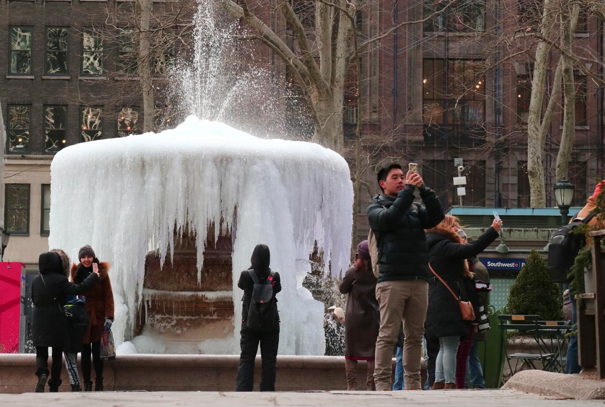 People take selfies in front of frozen fountain in New York City.