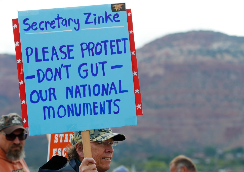 A man holds a sign in protest during Ryan Zinke's visit to Utah in 2017.