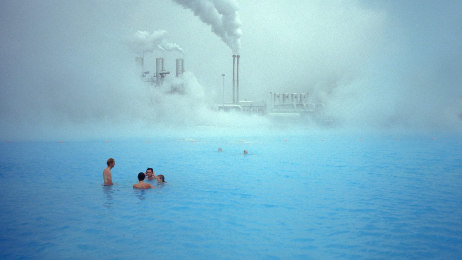 Icelandic bathers swim in front of a geothermal plant.