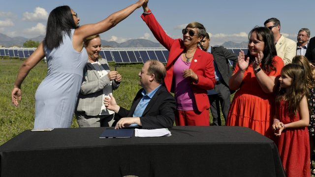 Representative Dominique Jackson and Senator Angela Williams High five after Governor of Colorado Jared Polis signs a climate action bill into law.