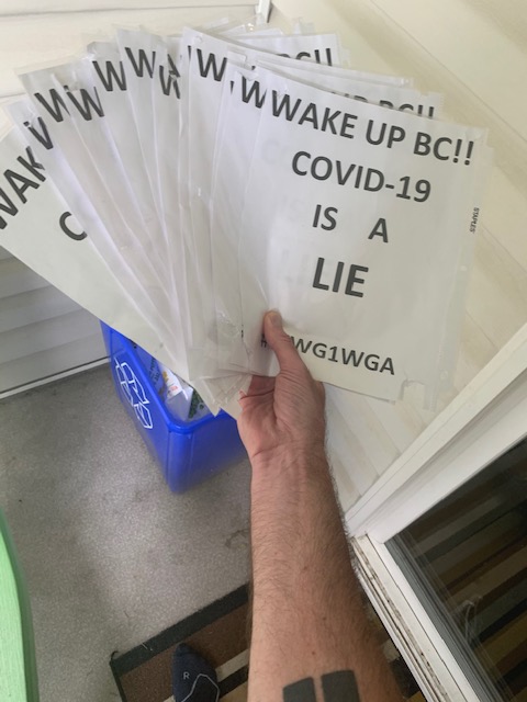 A photo of Walters holding COVID conspiracy signs above a recycling bin.