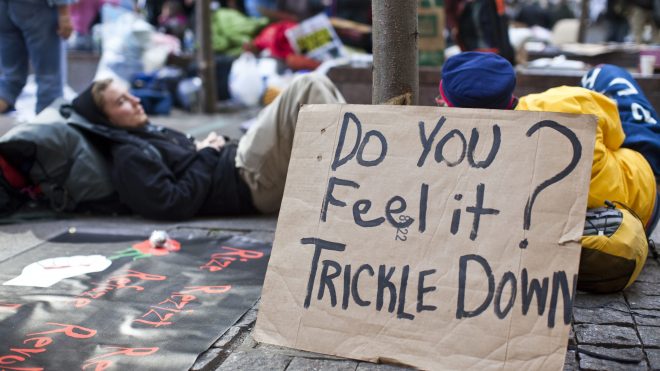 A photo shows protesters sleeping in Zuccotti Park next to a sign that says "Do you feel it trickle down?"