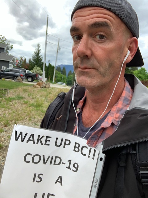 A selfie of Tim Walters with a sign saying COVID-19 is a hoax.