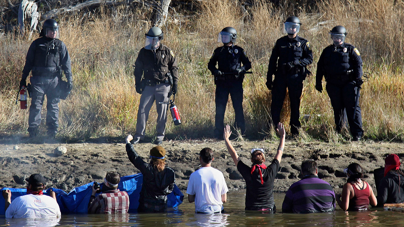 DAPL protestors wading in a creek confront police in riot gear