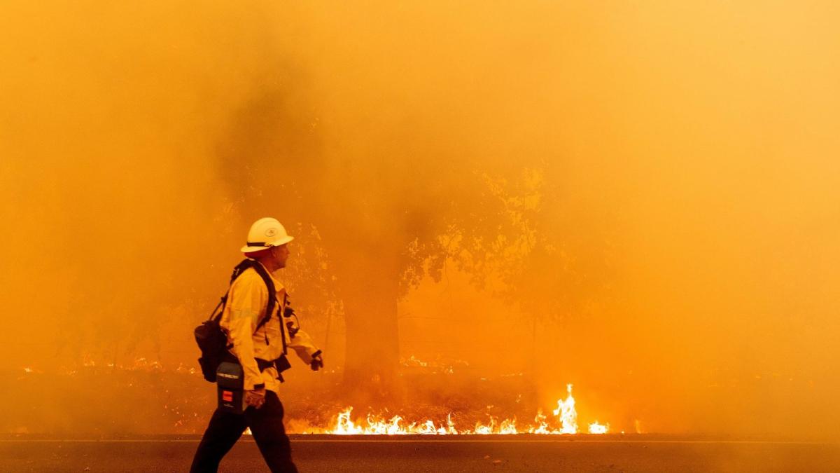 A Pacific Gas and Electric firefighter walks down a road as flames approach in Fairfield, California during the LNU Lightning Complex fire on August 19, 2020.