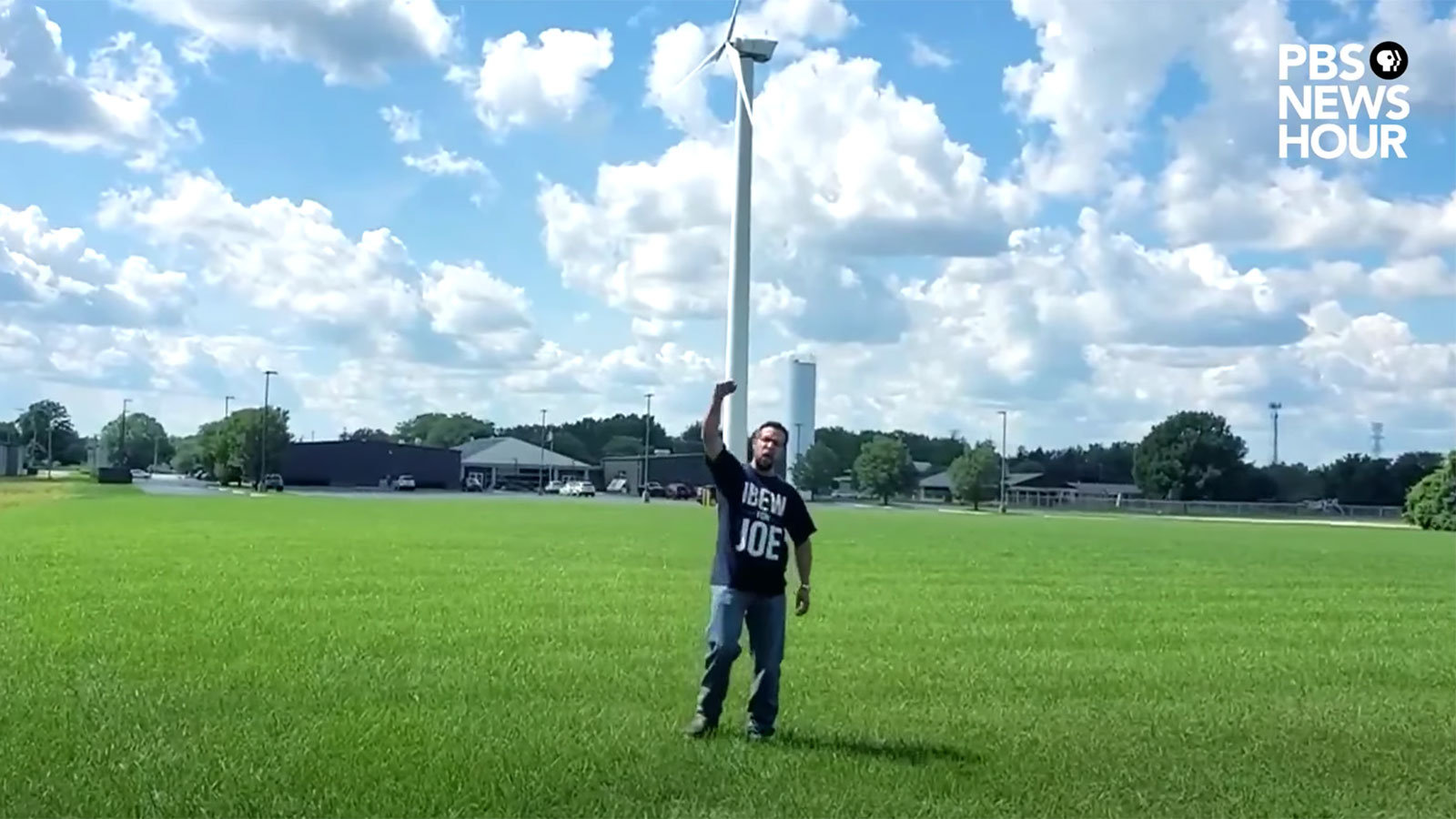 A man turns away from a large wind turbine and raises his fist in support of Joe Biden