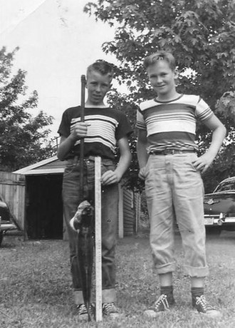 A black-and-white photo of two boys on a farm with a large fish.