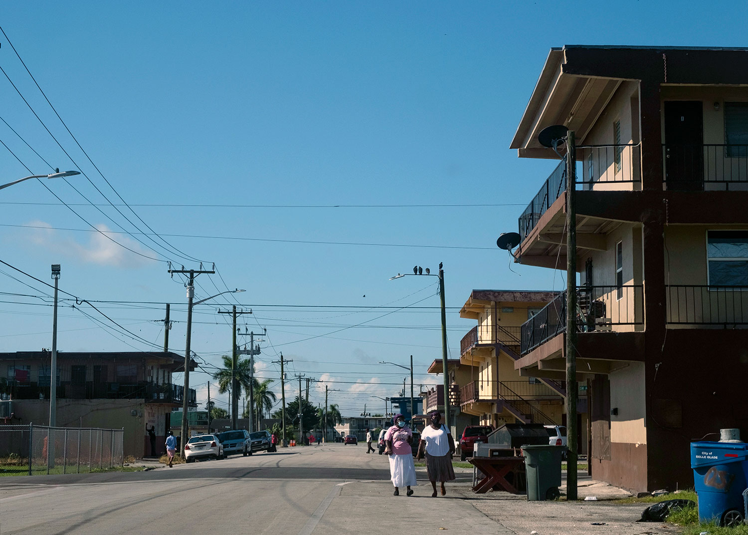 Belle Glade residents wearing masks walk down a street off of Martin Luther King, Jr. Boulevard, as COVID infection rates in Florida reach record highs (left).