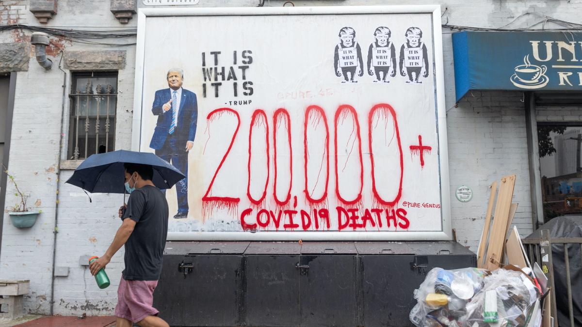 A man walks by graffiti of Trump and lettering reading "200,000 COVID-19 deaths."