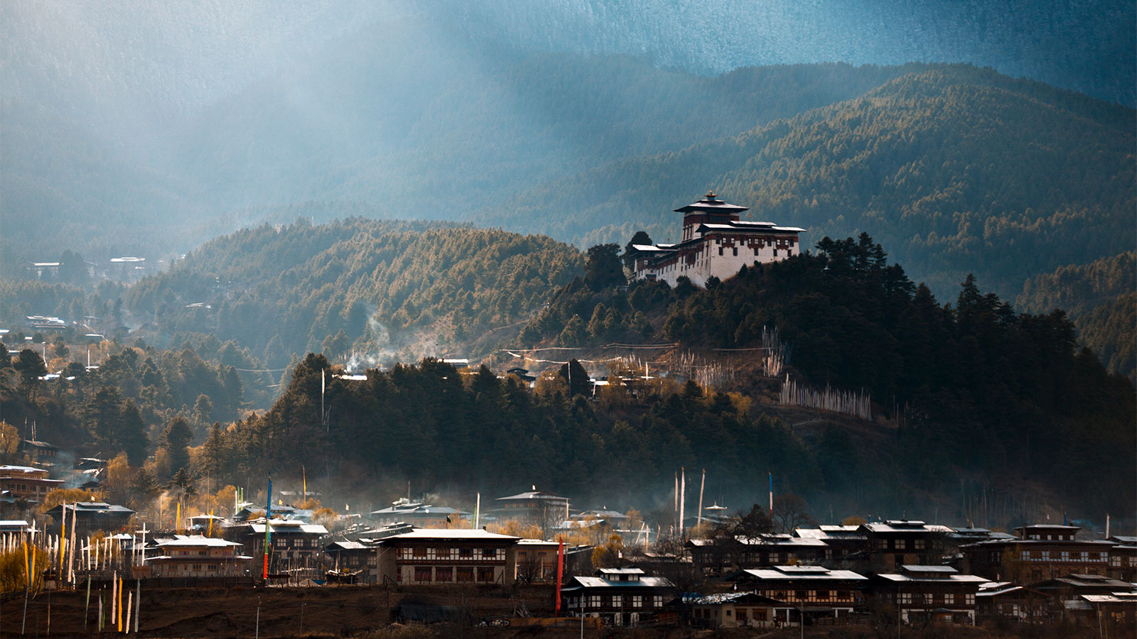 A photograph of Jakar town and Dzong in Bhutan, with rays of sunlight breaking through the morning mist.