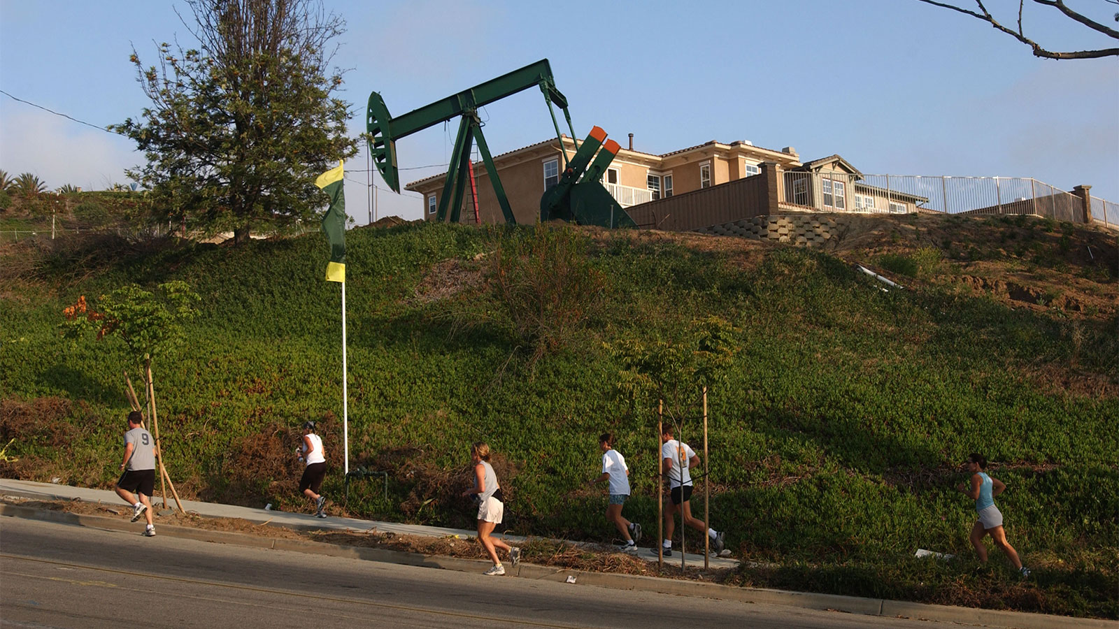 A group of joggers passes an oil well pumping next to residential units under construction in residential California