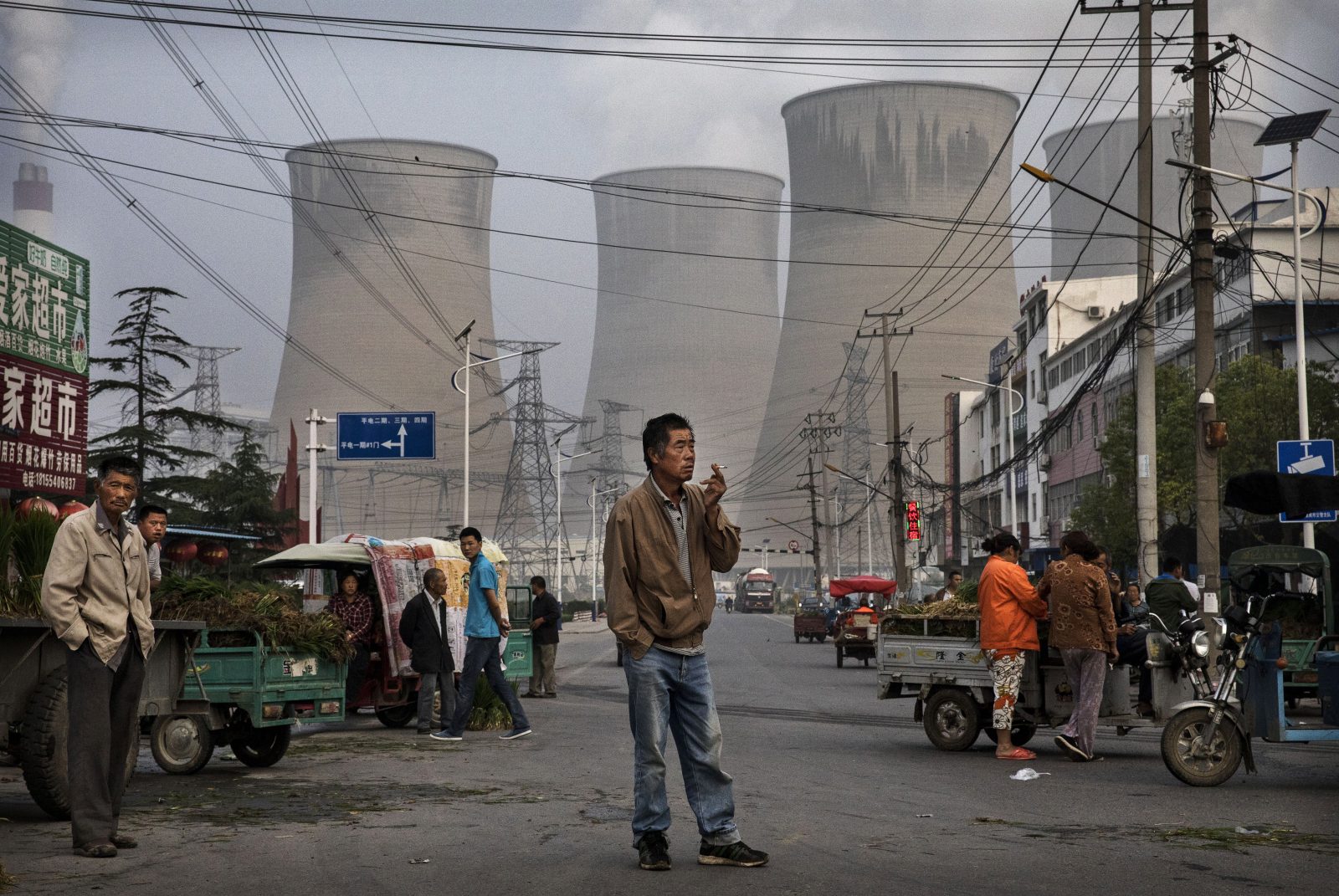 Street vendors and customers are gathered at a local market in front of a coal plant.
