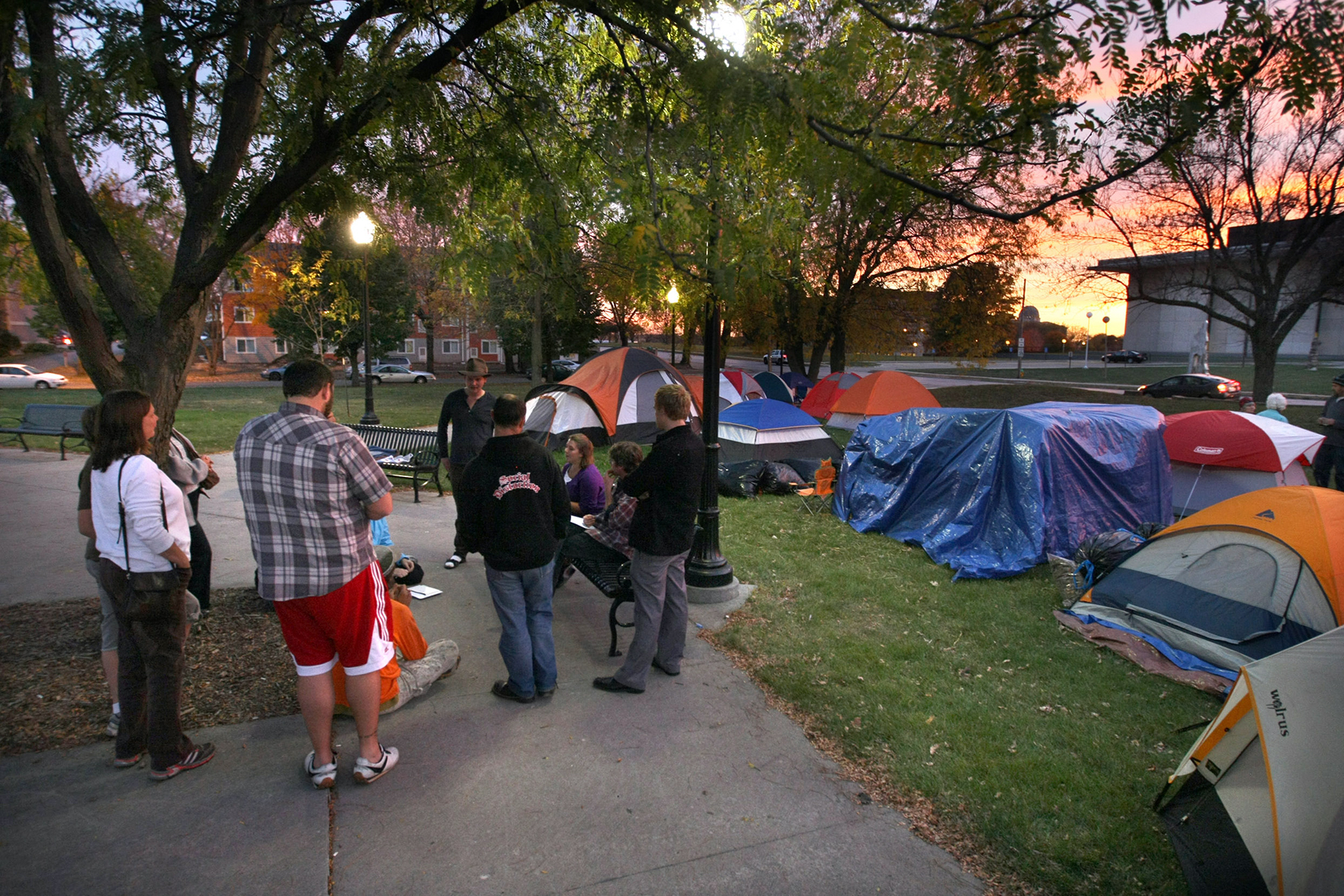 A photo of a small circle of people on the left, a large green lawn with tents on the right