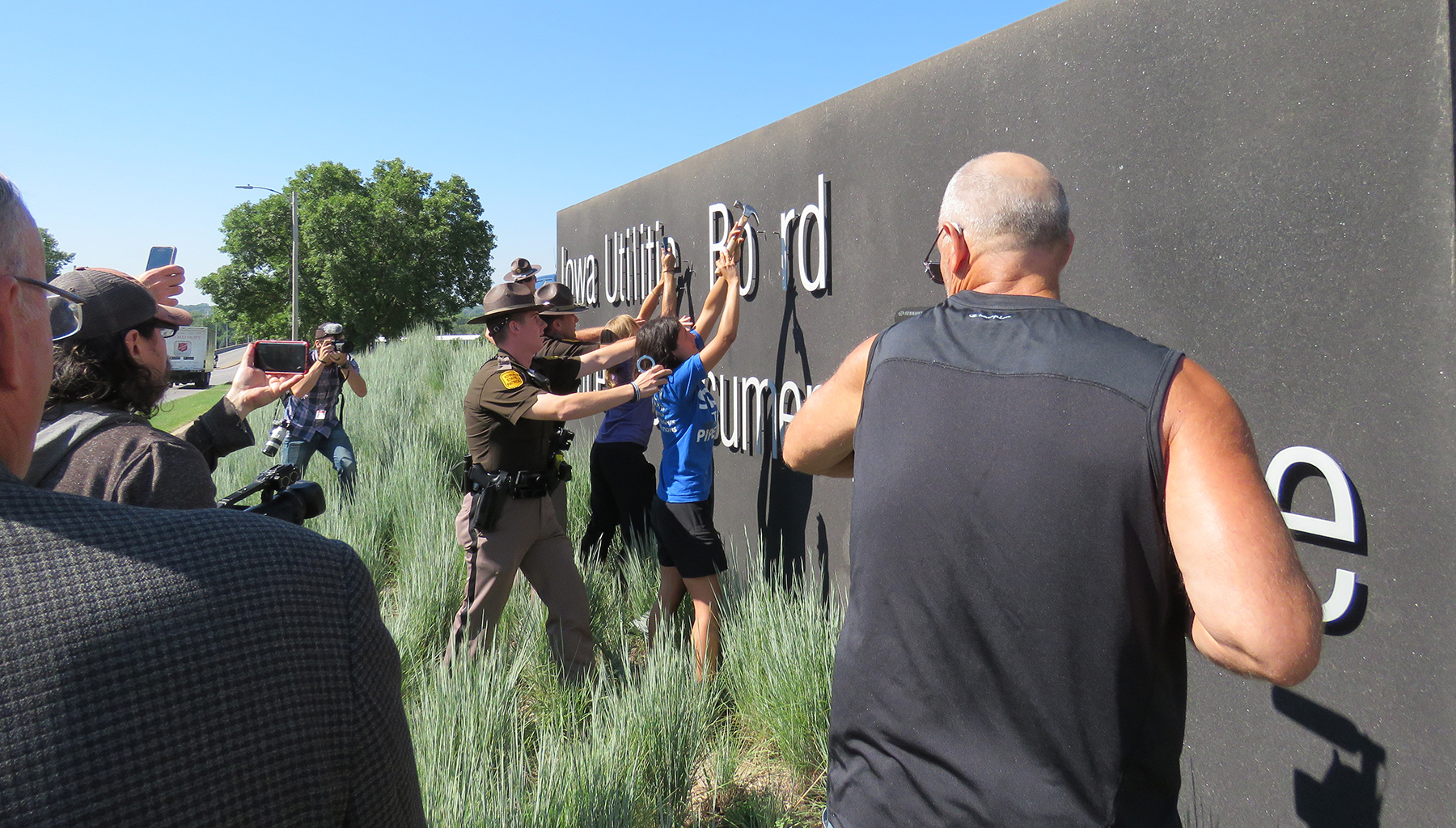 A photo of a uniformed law enforcement officers with hands on a woman's shoulders as she places both hands on a large gray sign