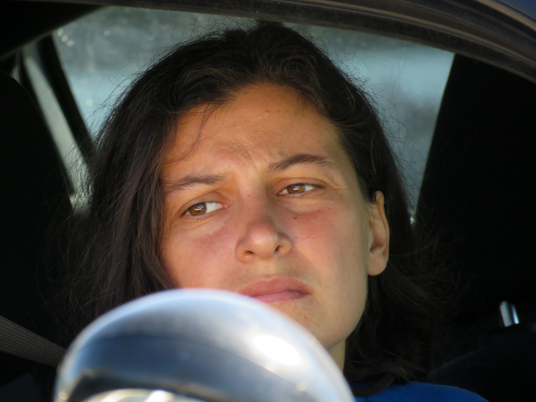 A close-up of Ruby Montoya (a woman with long brown hair) looking somber while sitting inside a vehicle