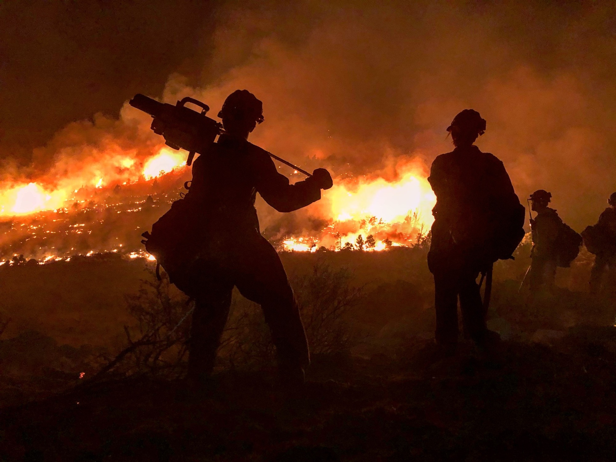 Fire blazing in the backgroud with two hot shot silhouetted in the foreground as they attempt to fight California wildfires