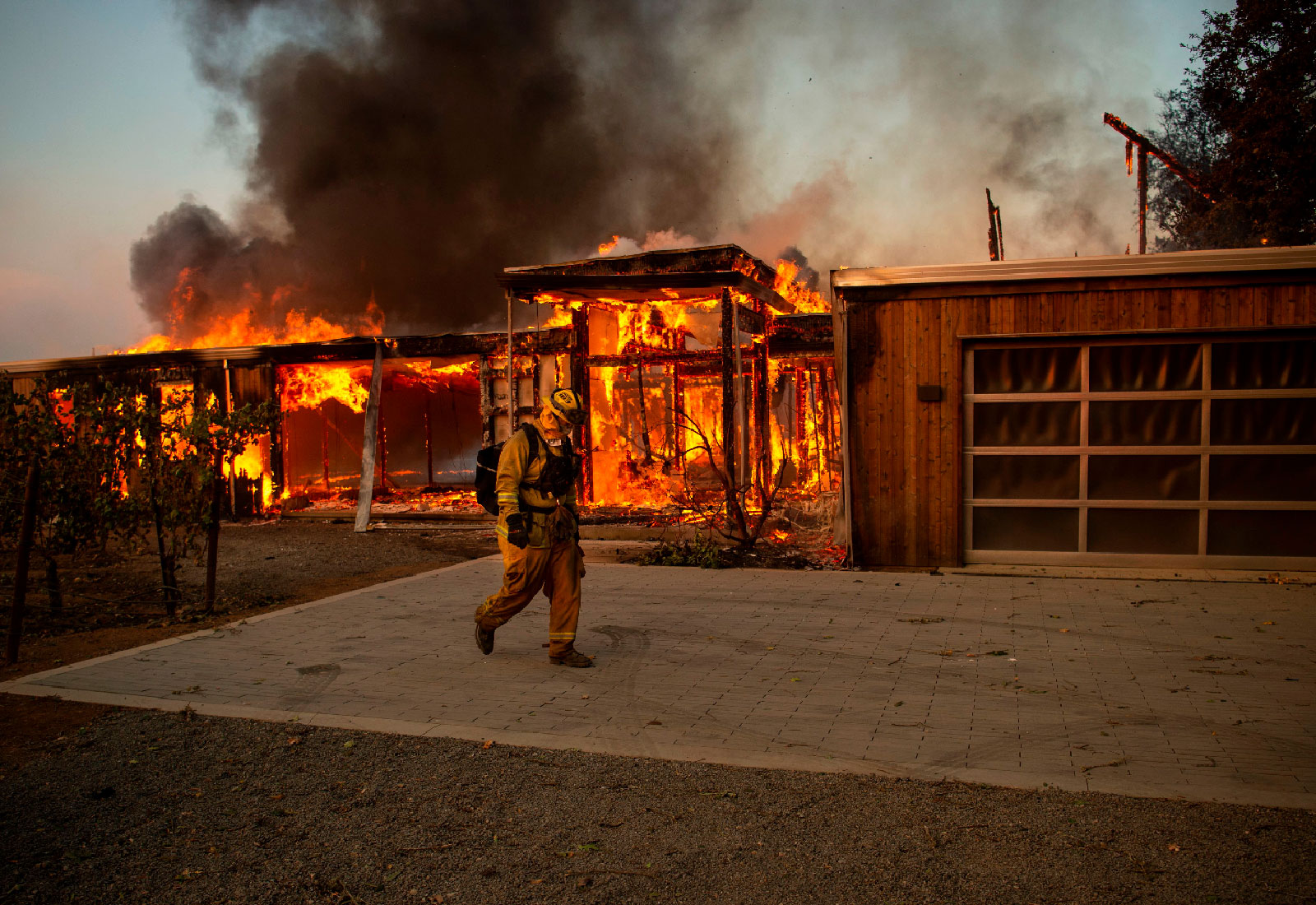 A firefighter walks past a burning house