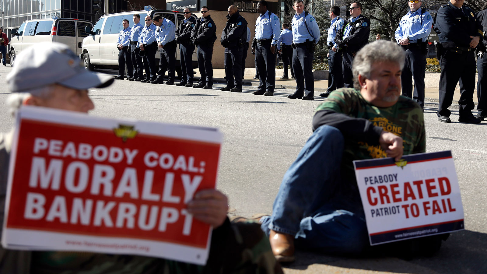 Two men holding signs protesting Peabody Energy with police in the background