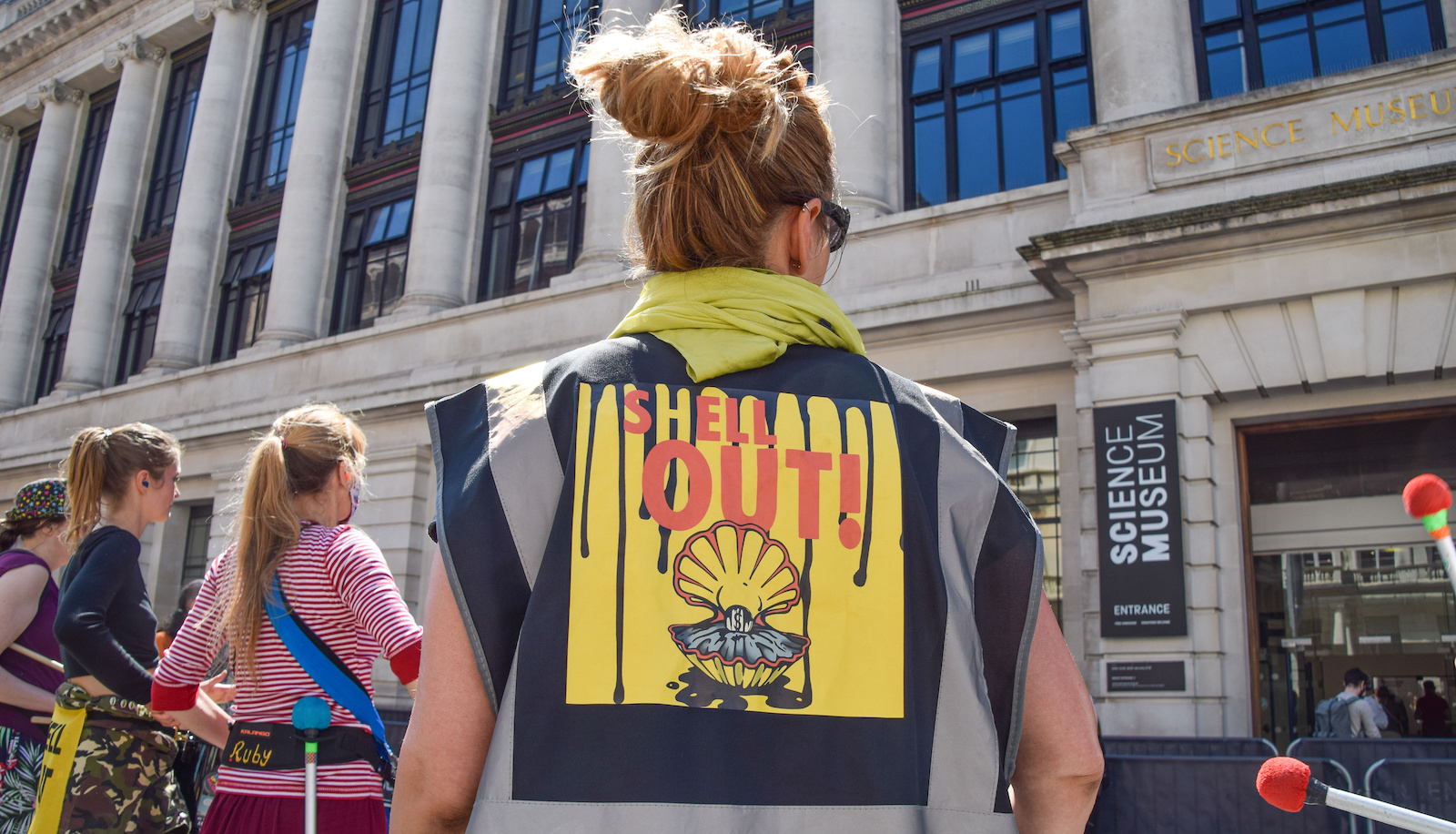 Woman stands outside UK science museum with shirt that says SHELL OUT