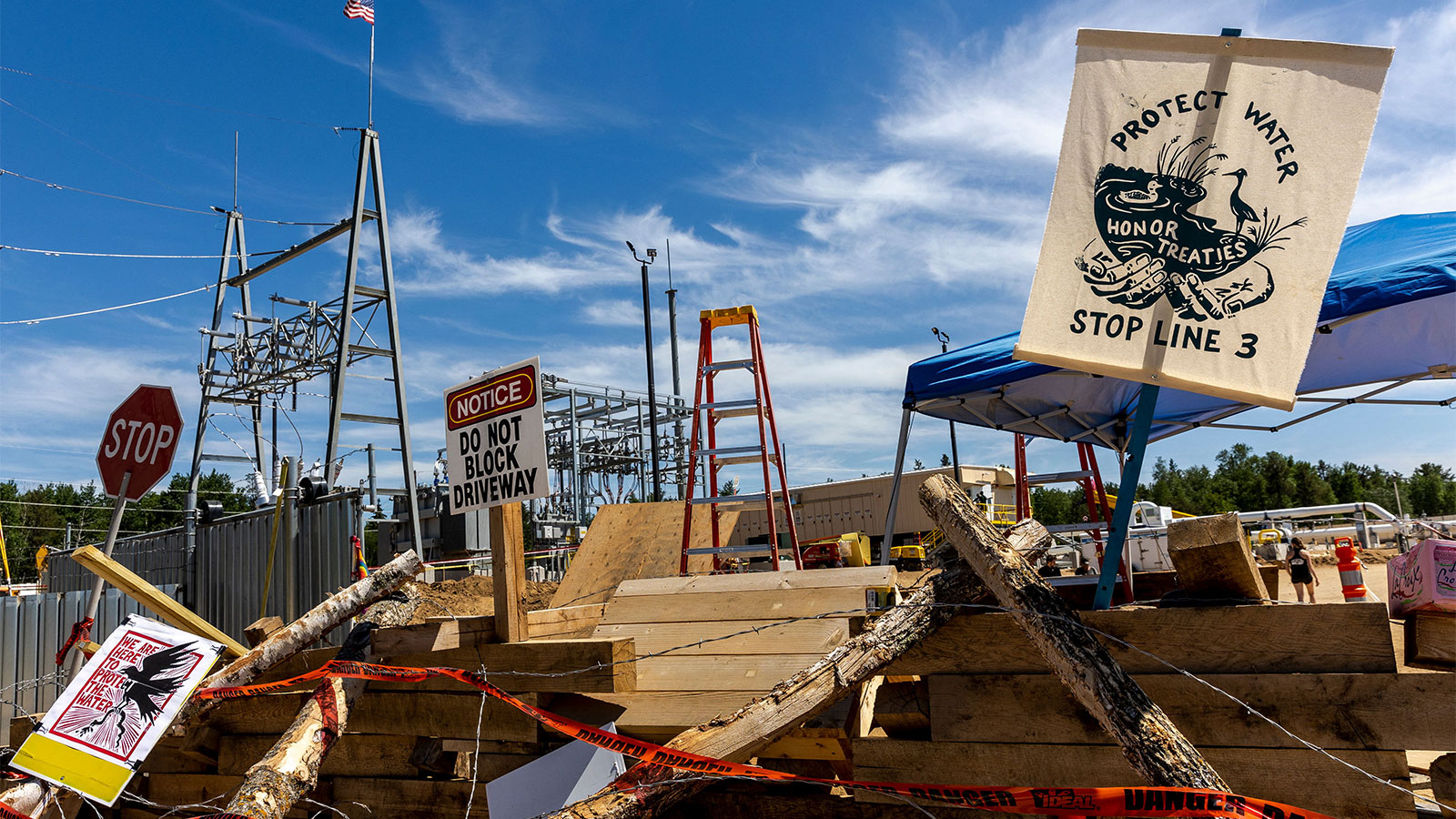 Protest signs in front of machinery and materials at the site of the Line 3 pipeline